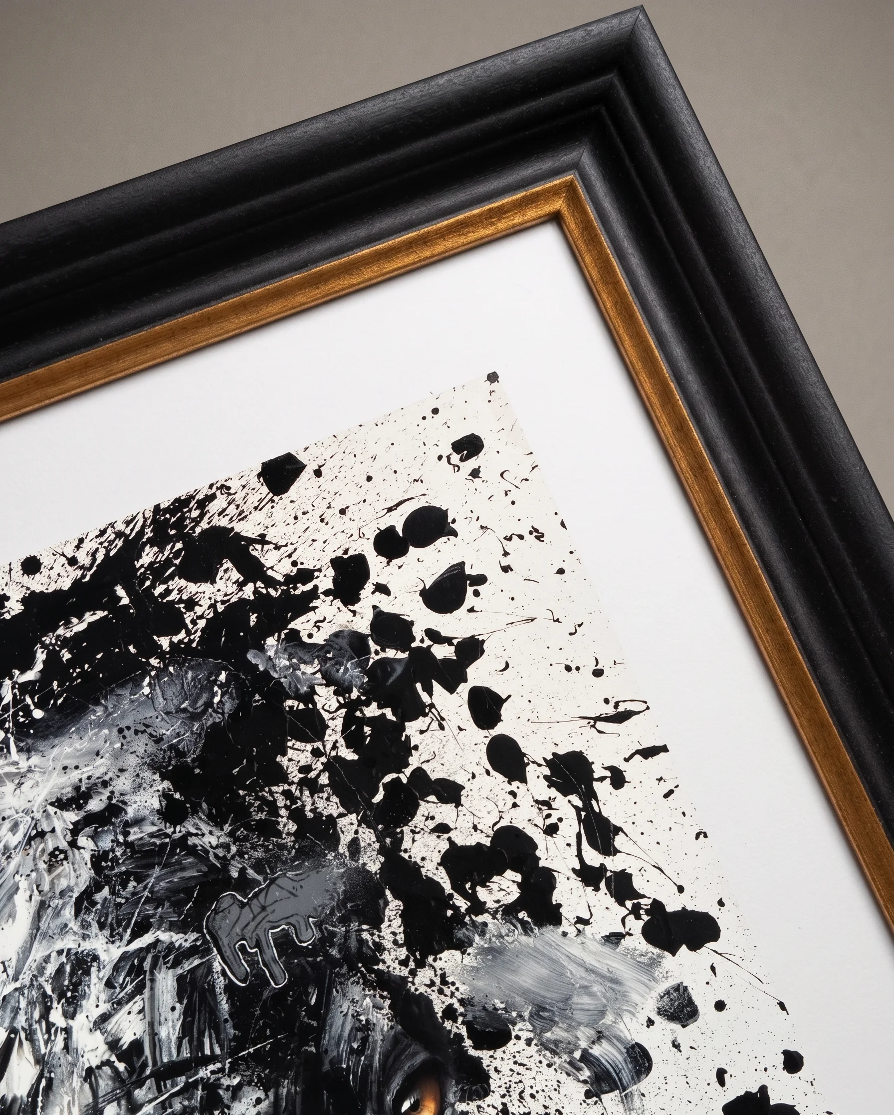 Détail d'une œuvre à l'encre noire jetée sur papier blanc, dans un cadre noir bordé d'une fine bande dorée