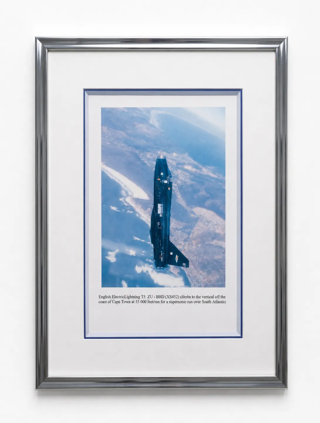 Photographie d'un avion en vol vertical, encadrée dans un cadre argenté avec triple passe-partout