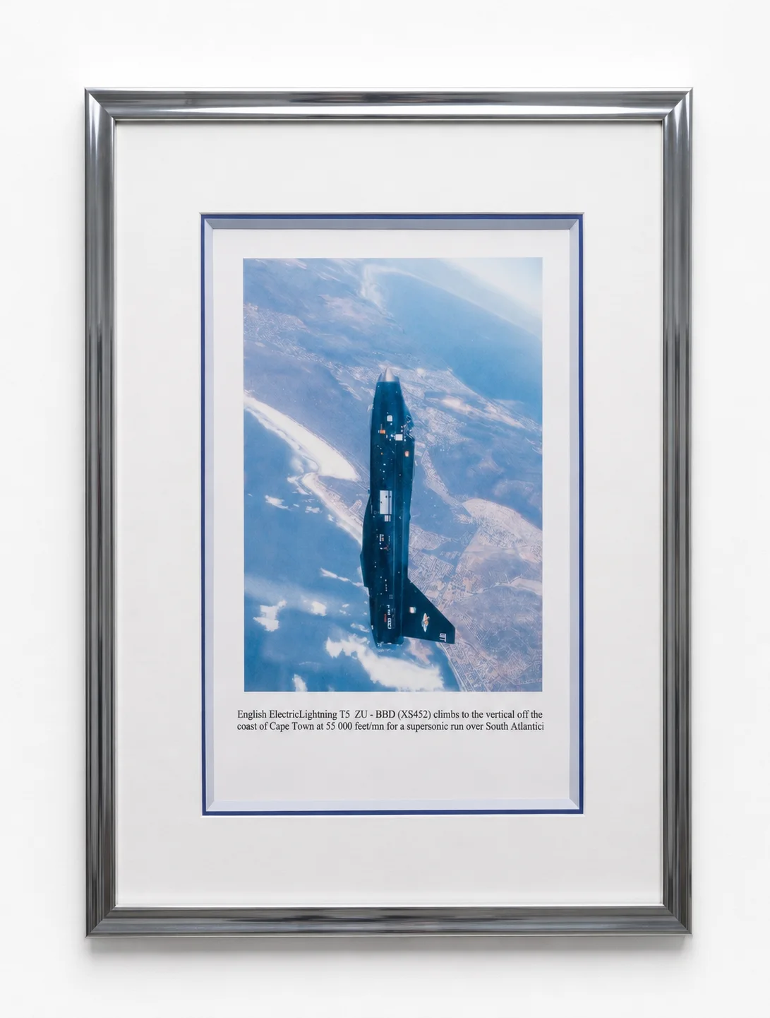 Photographie d'un avion en vol vertical, encadrée dans un cadre argenté avec triple passe-partout